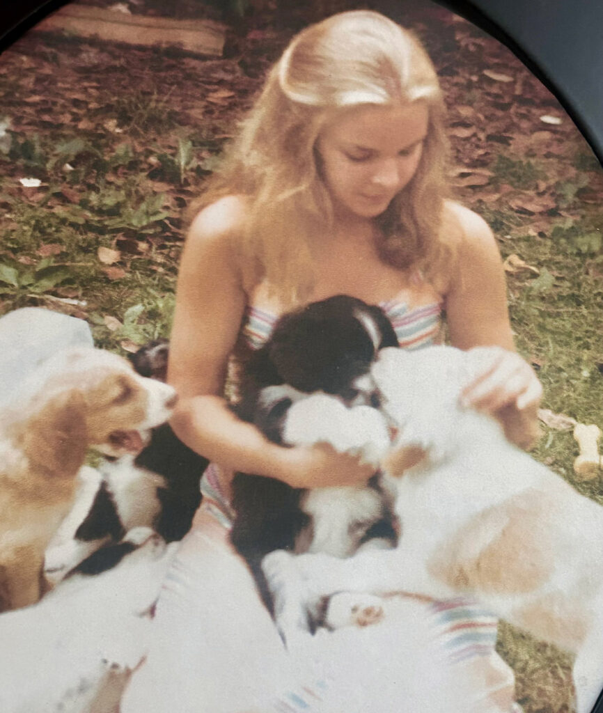 A woman smiles while holding a dog in one arm and a puppy in the other